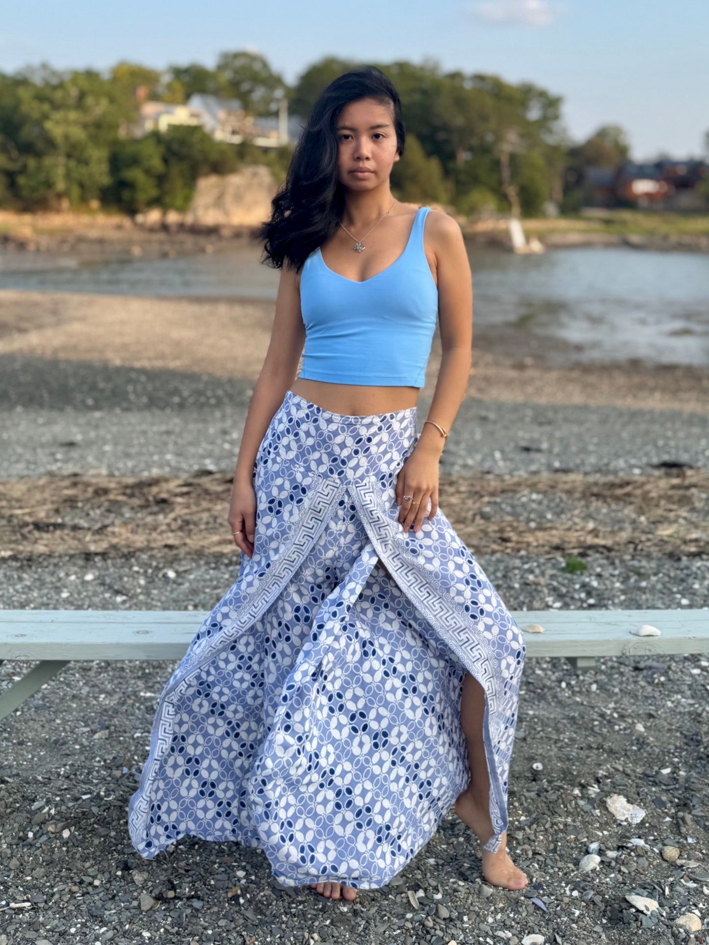 Model wearing high slit beach pants in blue and white print, standing on a rocky beach.