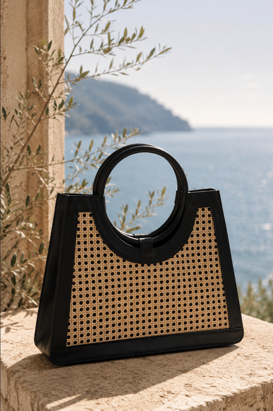 Black and beige handbag with woven pattern on a stone ledge with a scenic background
