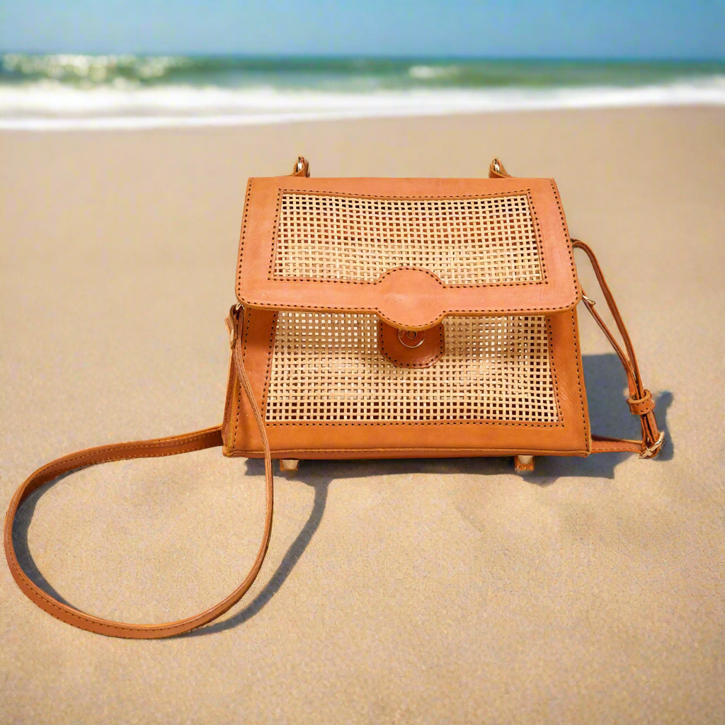 Maya Rattan bag with crossbody strap on a beach.