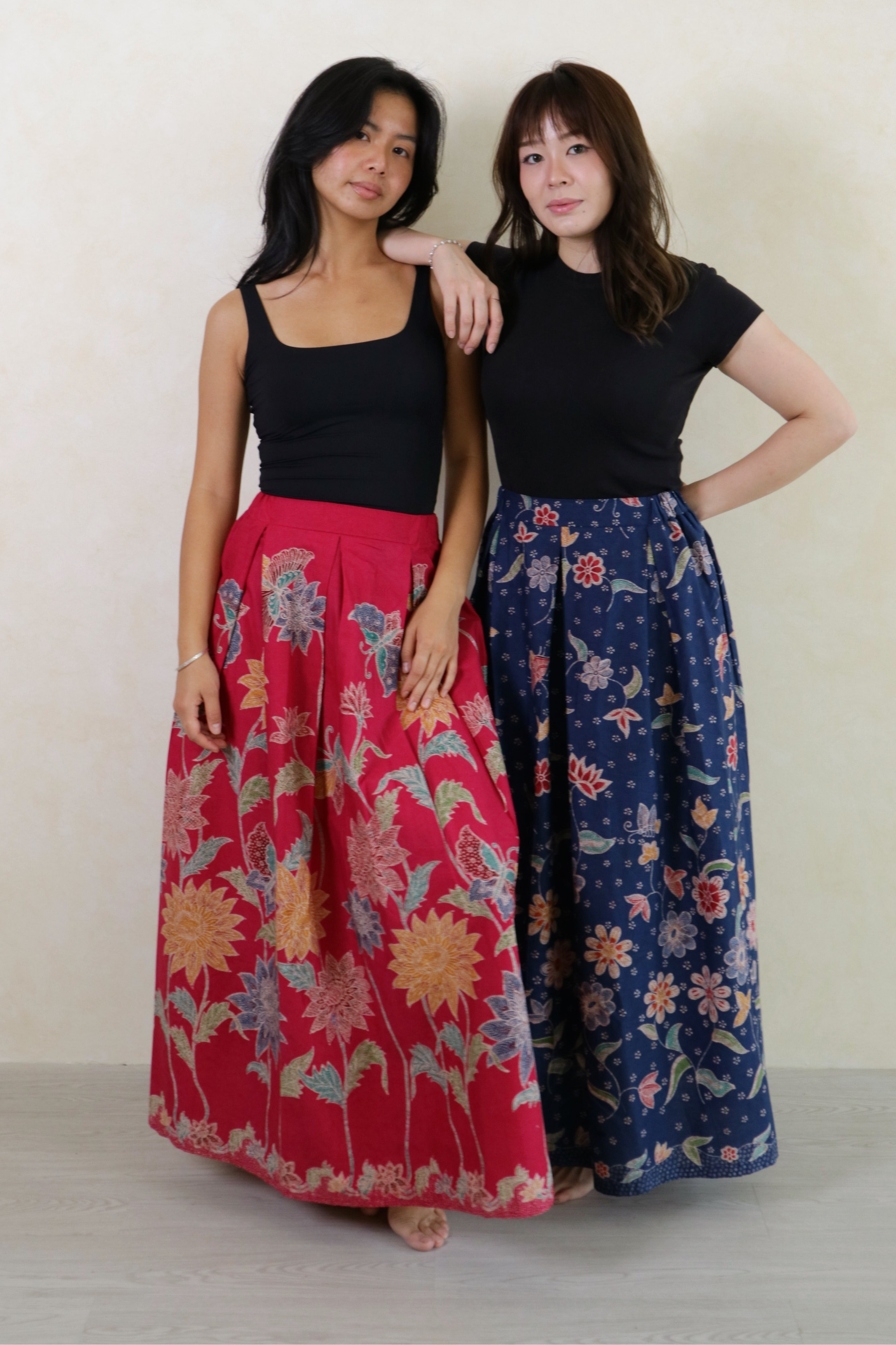 Two women wearing long floral patterned skirts.