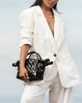 Model in white linen suit carrying black Nara Bag