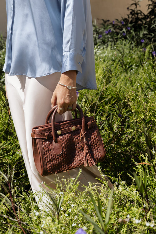 Model wearing blue shirt carrying brown Kirana Bag in a grassy field