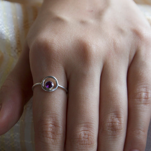 Hand wearing a silver ring with a purple gemstone on a textured fabric background