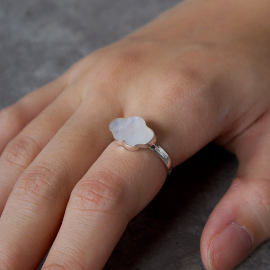 Hand wearing a silver ring with a clear stone on a gray background