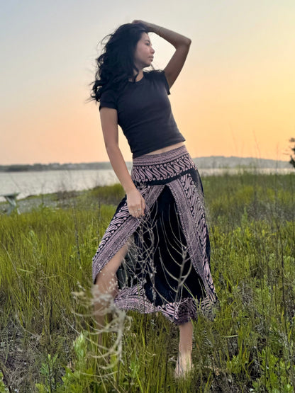 Model wearing black and pink patterned Hanna capri pants with front slits, standing in a grassy filed near the ocean.