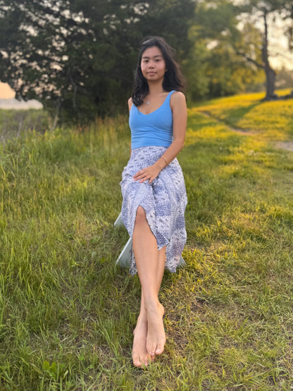 Model wearing blue and white capri-length Hanna Pants, sitting on a bench in a grassy field. 