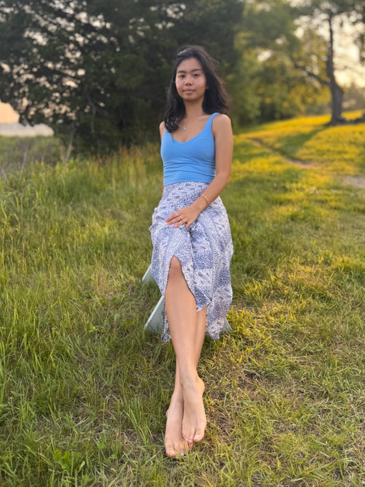 Model wearing blue and white capri-length Hanna Pants, sitting on a bench in a grassy field. 