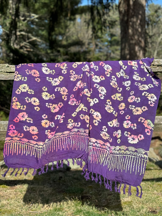 purple bali sarong with flower patterns draped over a fence.