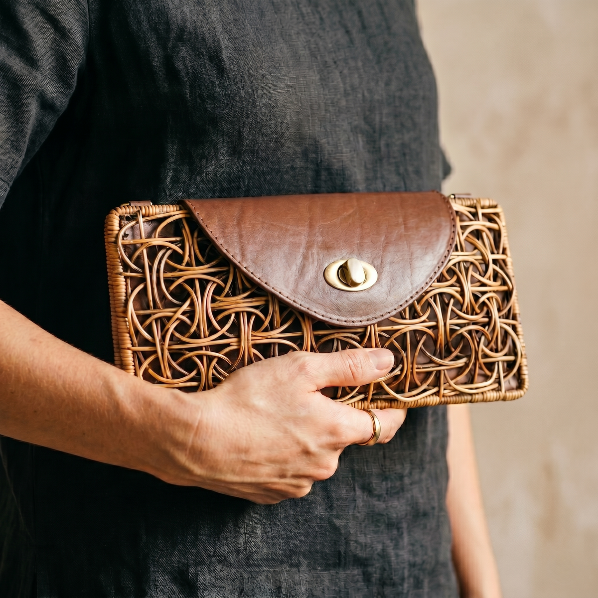 Person holding a brown woven clutch bag with a gold clasp.